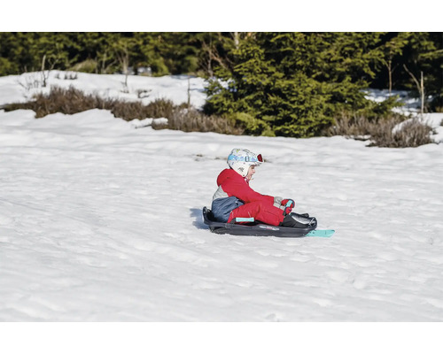 Kind sitzt auf einem Schlitten im Schnee