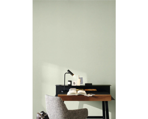 Arbeitszimmer mit Schreibtisch, Lampe und Stuhl vor hellgrüner Wand