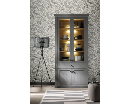 Wohnzimmer mit grauem Vitrinenschrank, Stehlampe und gemusterter Tapete.