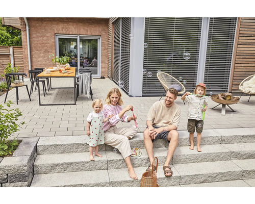 Familie spielt mit Seifenblasen auf einer Terrasse mit Steinplatten und Treppe