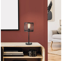 Schwarze Tischleuchte mit Lampenschirm aus Metallgitter auf einem Holztisch.