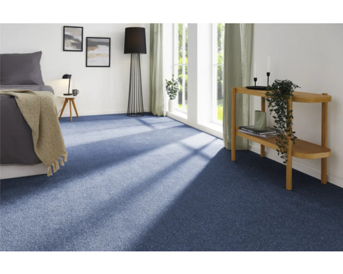 Blaues Teppichzimmer mit Bett, Nachttisch, Stehlampe und Fenster für eine helle, geräumige Atmosphäre