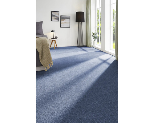 Helles Schlafzimmer mit blauem Teppichboden, Bett, Beistelltisch und Stehlampe.