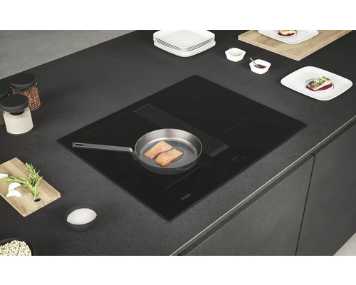 Schwarzes Haier Induktionskochfeld mit integriertem Dunstabzug in einer Küchenarbeitsplatte mit einer Pfanne mit Lachs.
