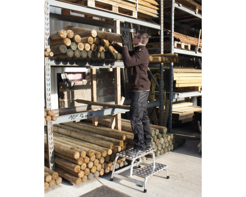 Eine Person steht auf einer Trittleiter und entnimmt Rundhölzer aus einem Regal.