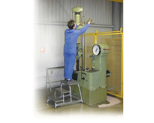 Eine Person bedient eine Materialprüfmaschine von einer dreistufigen Trittleiter aus.