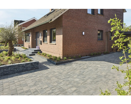 Gepflasterte Auffahrt vor einem Backsteinhaus mit Gartenbeeten.
