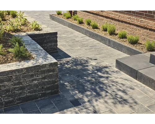 Außenaufnahme eines Gartens mit Pflastersteinen, einer Mauer und Bepflanzung.