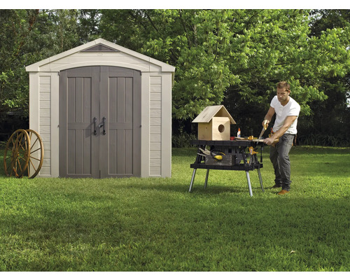 Gartenszene mit Gerätehaus und einer Person, die an einer Werkbank arbeitet