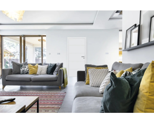 Helles Wohnzimmer mit grauen Sofas, Kissen und einer weißen Tür.