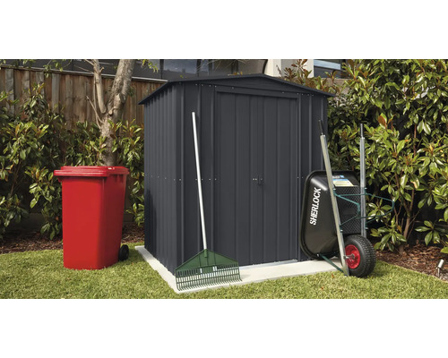 Gartenszene mit Gerätehaus, Mülltonne, Schubkarre und Rechen im Außenbereich.