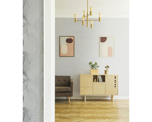 Wohnzimmer mit grauer Blättertapete, braunem Sofa, Kommode und goldener Lampe