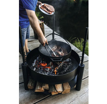 Person bereitet Steaks auf einer Feuerstelle im Freien zu.