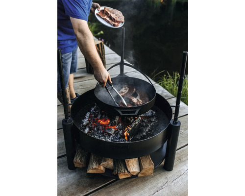 Person bereitet Steaks auf einer Feuerstelle im Freien zu.