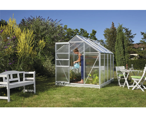 Gewächshaus im Garten mit Frau, die Pflanzen gießt