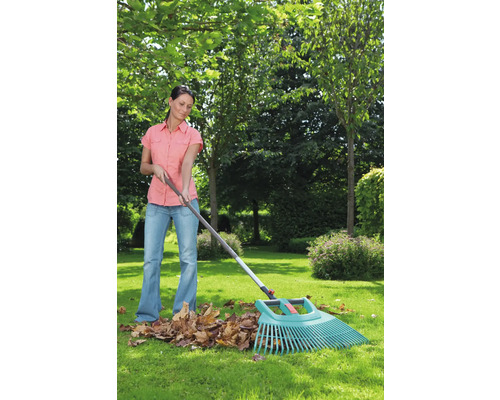 Frau beim Zusammenrechen von Laub mit einem Laubbesen im Garten.