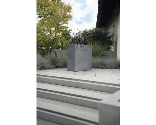 Quadratischer Pflanzkübel aus Beton im Außenbereich auf einer Terrasse mit Treppe.