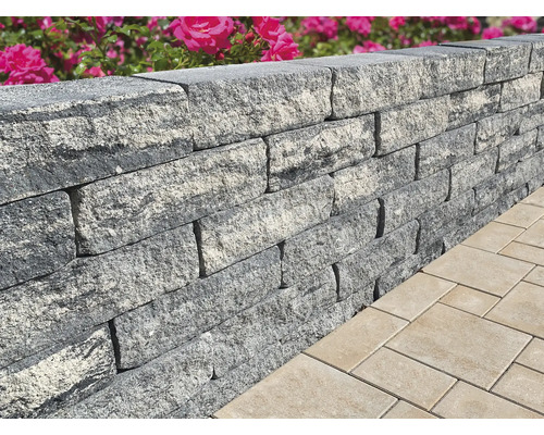 Nahaufnahme einer grauen Gartenmauer aus Steinen neben Pflastersteinen