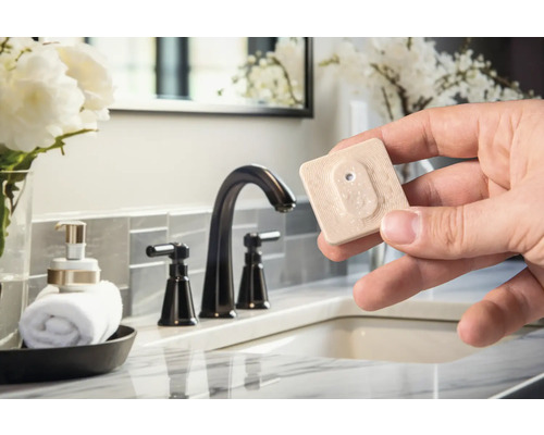 Szene eines Badezimmers mit einem Handtuchhalter, einer Seifenspenderflasche, einem Waschbecken und einer Hand, die einen Feuchtigkeitssensor hält.