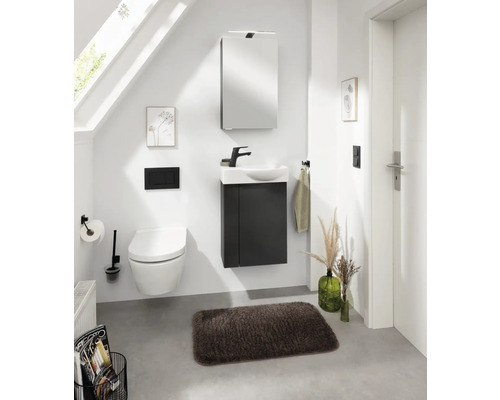 Badezimmer mit Toilette, Waschtischunterschrank, Spiegelschrank und Accessoires unter einer Dachschräge
