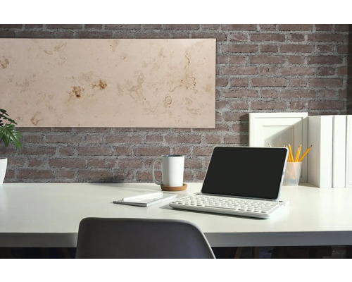 Schreibtisch mit Tablet, Tastatur, Tasse und Dekorationspaneel vor einer Backsteinwand