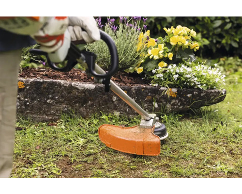 Gartenszene mit Rasentrimmer in Aktion, umgeben von Blumenbeet