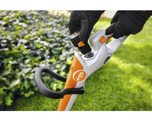 Eine Person setzt einen Akku in einen Akku-Rasentrimmer ein.