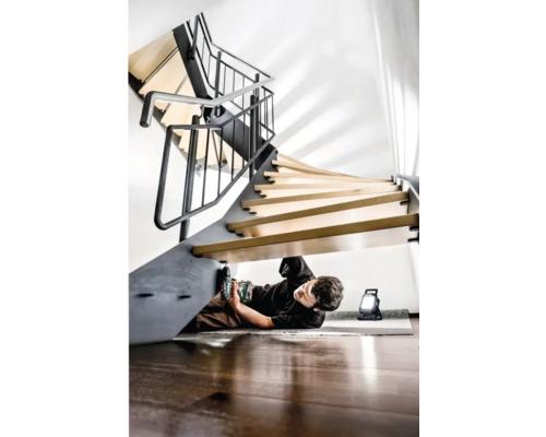 Mann montiert Wendeltreppe mit Akkubohrer und Arbeitsleuchte