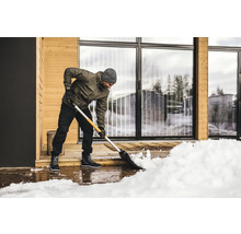 Eine Person schaufelt Schnee vor einem Haus mit einer Schneeschaufel.