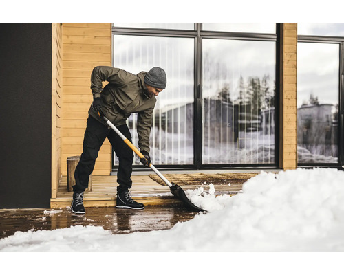 Eine Person schaufelt Schnee vor einem Haus mit einer Schneeschaufel.