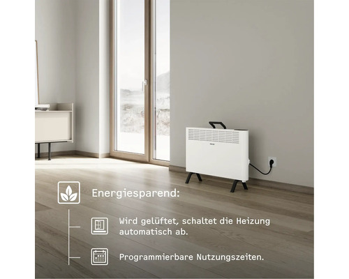 Weißer Elektroheizkörper auf Füßen in einem Raum mit Holzboden und Fenstern.