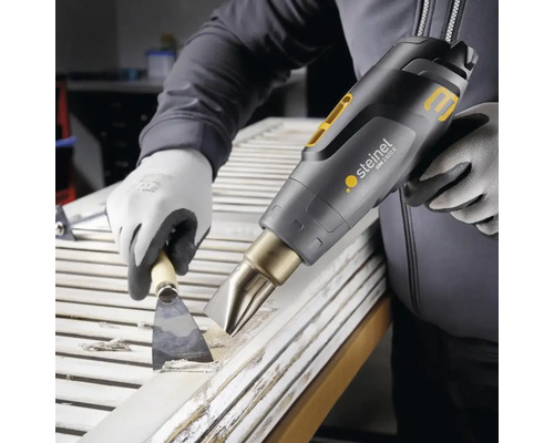 Eine Person entfernt mit einer Heißluftpistole und einem Spachtel Farbe von einer Tür.