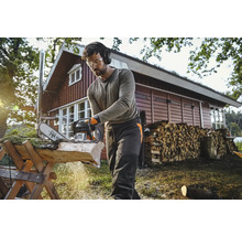 Mann mit Schutzbrille und Gehörschutz sägt Holz mit einer Motorsäge auf einem Holzbock im Freien.