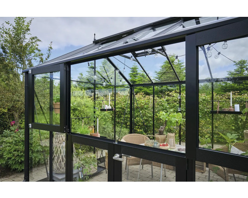 Gewächshaus mit Glaswänden und Metallrahmen, eingerichtet mit Tisch und Stühlen.