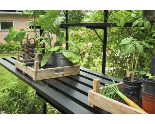 Gartenarbeitstisch mit Pflanzen, Werkzeugen und Pflanzgefäßen in einem Gewächshaus.