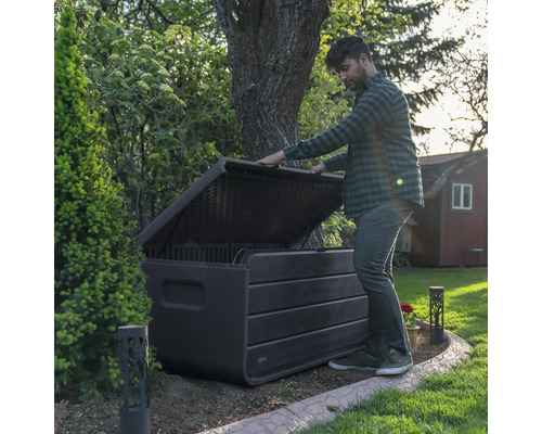 Mann öffnet eine wetterfeste Aufbewahrungsbox im Garten zur Aufbewahrung von Gartengeräten und Spielzeug