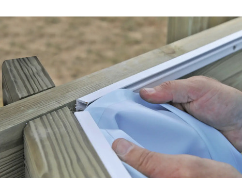 Eine Person montiert eine Sichtschutzfolie an einem Holzzaun.