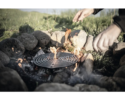 Feuerstelle mit Grillrost, umrandet von Steinen, mit Händen darüber