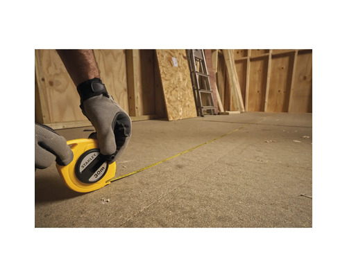 Person misst mit einem 30 Meter Rollbandmaß von Stanley einen Raum aus Holz aus.