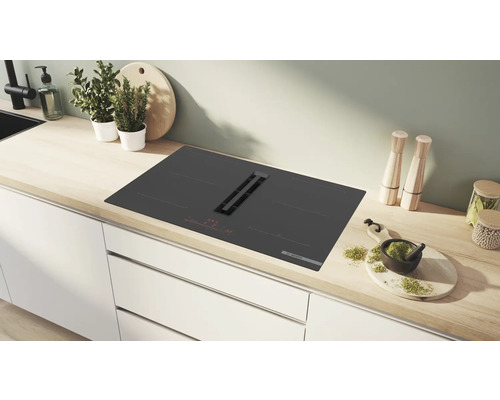 Schwarzes Kochfeld mit Dunstabzugshaube in einer hellen Küche.