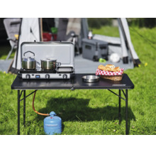 Campingszene mit Tisch, Gaskocher, Kochutensilien und Lebensmitteln vor Zelt