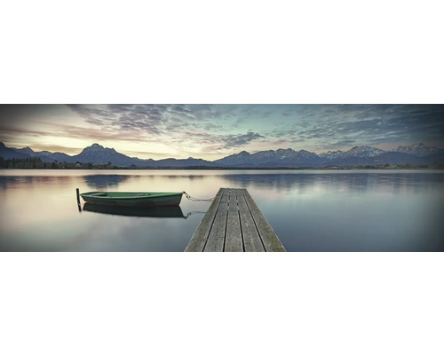 Leinwandbild Morgenstimmung 150x50 cm Ein ruhiger See mit einem Holzsteg und einem kleinen Boot vor einer Bergkulisse.