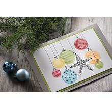 Dekorative Weihnachtskarte mit Christbaumkugel-Motiven und Tannenzweig auf einem Holztisch