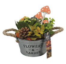 Blumenarrangement in einem Metalleimer mit der Aufschrift Blumen und Garten, zusammen mit dekorativen Pilzen und einem Tannenzapfen.