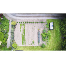 Luftaufnahme eines Gartens mit Gemüsebeeten und Gewächshaus