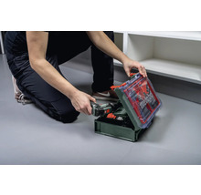 Eine Person hockt vor einem offenen Werkzeugkoffer mit Metabo Logo und hält einen Akkuschrauber.
