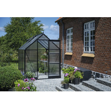 Gewächshaus mit geöffneter Tür in einem Garten neben einem Backsteingebäude.