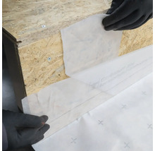 Anwendung einer Dichtfolie auf einer Holzoberfläche mit Handschuhen.