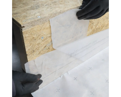 Anwendung einer Dichtfolie auf einer Holzoberfläche mit Handschuhen.