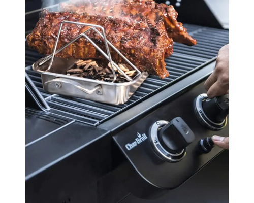 Grill mit Rippchen, Räucherbox und Holzschnipseln sowie Hand an einem Drehknopf